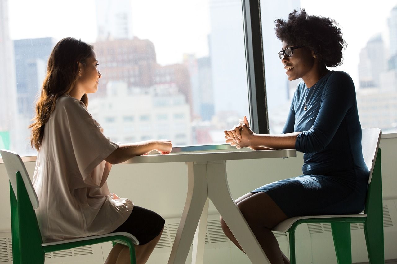 Two colleagues in conversation across a table by a window